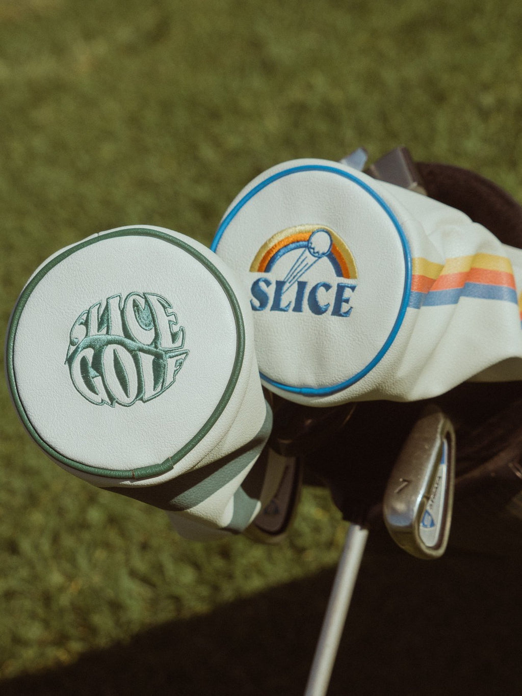 Driver head cover in white and green next to another in white, blue, orange and yellow.
